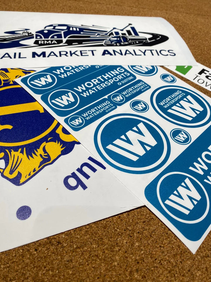 Assorted marine and watersports custom vinyl stickers, including Worthing Watersports branding, on cork surface.