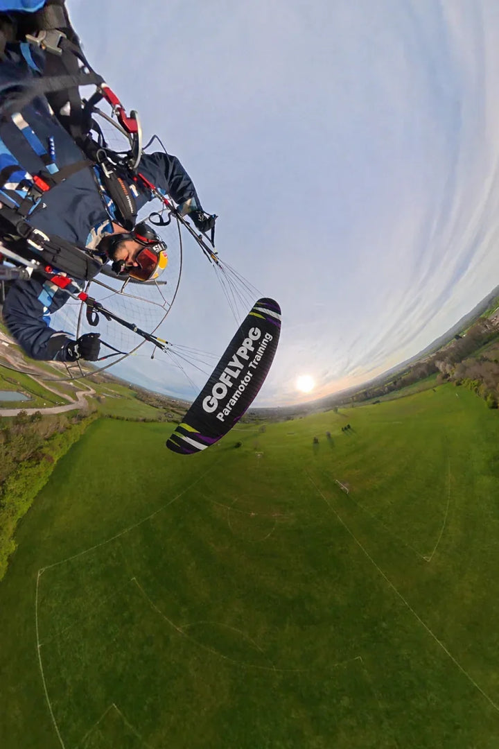 Paramotor pilot flying at sunset with printed fabric wing reading &