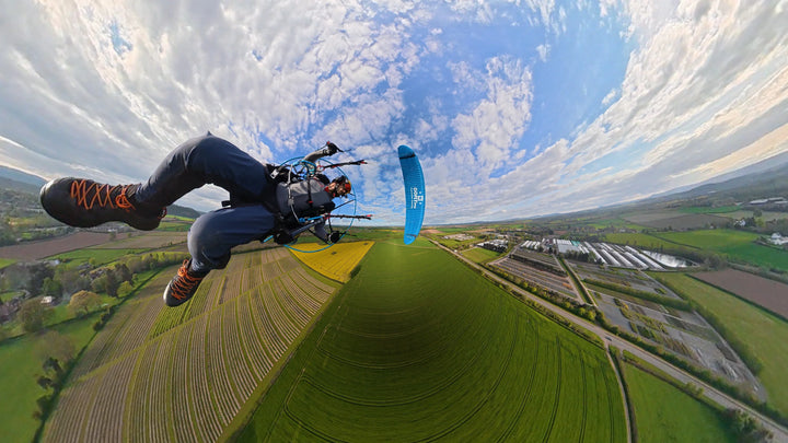 Paramotor pilot flying with blue fabric wing, open countryside below, UK made specialist print.